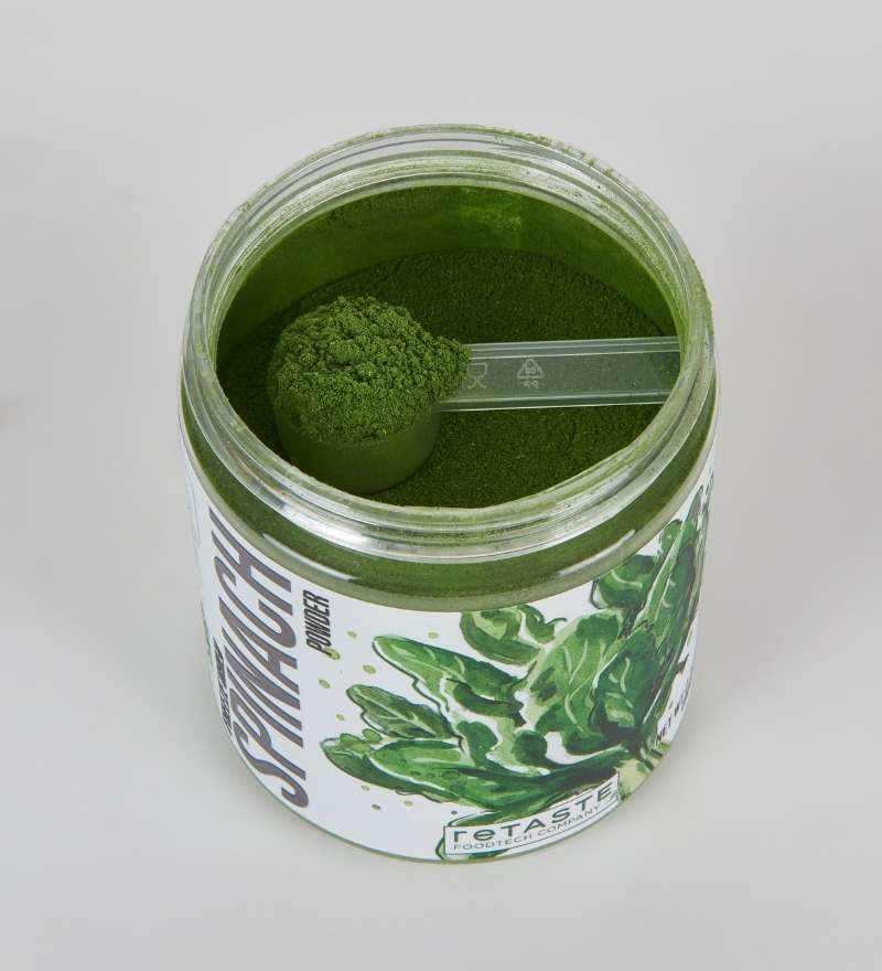 open jar of spinach powder from top with scoop inside